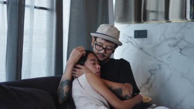 Genç Asyalı romantik bir çift. Evlerindeki kanepeye kıvrılmış dövmeleri var. 4K Yatay