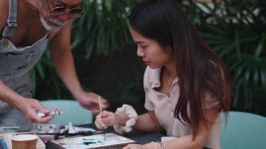 Resim eğitmeni, açık hava sanat dersi sırasında genç bir kız öğrenciye rehberlik ediyor. Sanatsal teknikleri paylaşıyor. 4K Yatay.