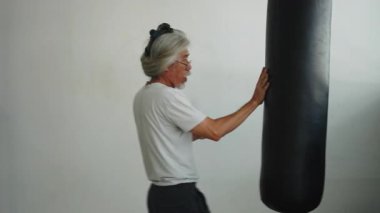 Yaşlı sporcu yumruk torbasını tekmeliyor ve yumrukluyor dövüş sanatları egzersizleri yapıyor - 4K Yatay