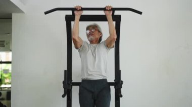 Asyalı son sınıf öğrencisi dayanıklılığını korumak için duvara monte edilmiş bir çubuğa barfiks çekiyor. 4K Yatay