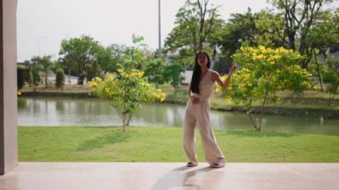 Genç bir Asyalı dansçı göl kenarındaki bir parkta koreografi yapıyor - 4K Yatay