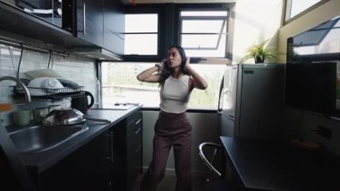 Modern mutfağında dans eden mutlu, uzun saçlı Taylandlı genç kadın - 4K Yatay