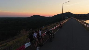 Motorcular barajdan gelen sakin su deposunun üzerinde çarpıcı gün batımını izliyorlar - 4K Yatay