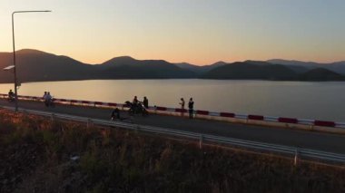 Gün batımında göl kenarında manzaralı bir yolda giden motosikletliler - 4K Yatay