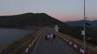 Gün batımında baraj yolunda yürüyen bir grup turist - 4K Yatay