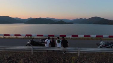 Motosiklet gezisinden sonra gölün üzerinde gün batımına hayran olan bir grup arkadaş - 4K Yatay