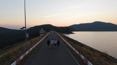 Güzel bir günbatımında baraj yolunda yürüyen bir grup turist - 4K Yatay