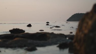 Sakin okyanus, arkasında bir ada olan pembe bir günbatımı gökyüzünü yansıtıyor - 4K Yatay