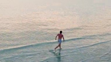 Gün batımında sığ sularda koşan genç bir adam bir İHA 'dan görüldü - 4K Yatay