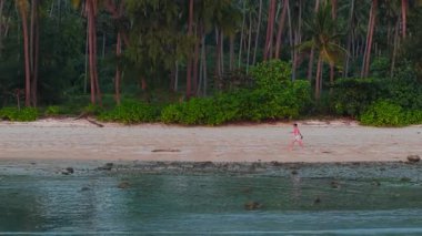 Gün batımında güzel bir plajda yürüyen genç adam denizden gelen bir İHA ile filme alındı - 4K Yatay