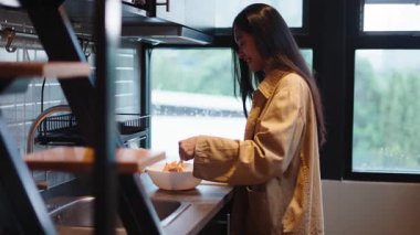 Genç bir kadın dikkatli bir şekilde besleyici bir yemek hazırlıyor. Taze malzemeleri bir kaseye karıştırıyor - 4K Yatay