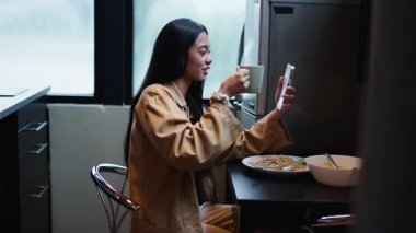 Genç ve mutlu bir kadın telefonun diğer ucundaki kişiyle kadeh kaldırırken bir video görüşmesi yapıyor - 4K Yatay