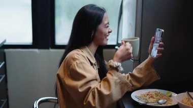 Asyalı bir kadın bir arkadaşıyla video görüşmesi yaparken bir fincandan su yiyip içiyor - 4K Yatay