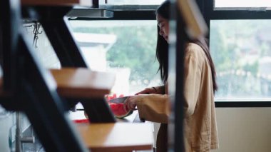 Asyalı bir kız mutfak tezgahında bıçakla olgun karpuz kesiyor - 4K Yatay
