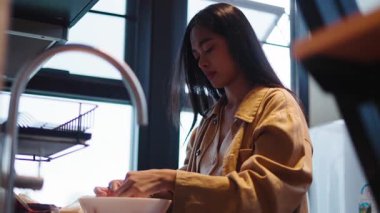 Genç bir kadın büyük pencereli, parlak bir mutfakta sağlıklı bir yemek hazırlıyor - 4K Yatay