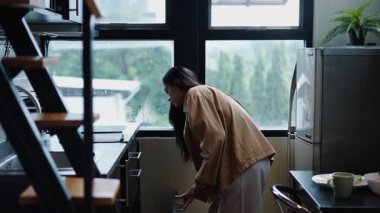 Taze yemek hazırlayan genç kadın, pencerenin yanındaki karpuzu çıkarmak için buzdolabını açıyor. 4K Yatay