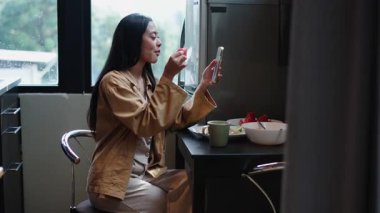 Genç Asyalı kadın karpuz yerken video çekiyor ve akıllı telefonuyla arkadaşına yemek gösteriyor - 4K Yatay