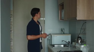 Genç Yetişkin Adam Modern Mutfakta Mikrodalga Fast Food 'u ısıtırken Akıllı Telefon Ekranına Bakıyor - 4K Yatay