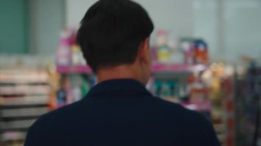 Market koridorunda yürüyen genç Asyalı adam çeşitli raflardan yiyecek arıyor ve seçiyor - 4K Yatay