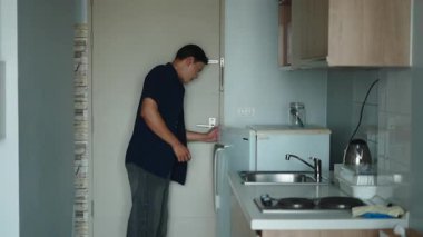 Genç Asyalı bir adam mutfak dolabında taze erzak depoluyor - 4K Yatay