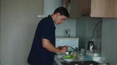 Genç Asyalı erkek sikkeci besleyici bir yemek hazırlarken taze sebzeleri dikkatlice doğruyor - 4K Yatay