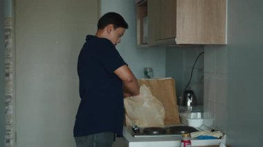 Mutfak tezgahında duran genç adam, sürdürülebilir bir kese kağıdından taze paketleri dikkatlice açıyor - 4K Yatay