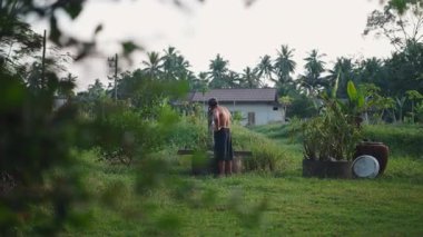 Güneydoğu Asyalı çiftçi bahçesinde bir su bidonuyla bitkileri suluyor - 4K Yatay