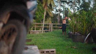 Şortlu Asyalı çiftçi ve bahçesindeki çıplak gövde sulama bitkileri - 4K Yatay