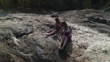 Anne ve kızı dağ yolunda yürürken çağlayan şelalenin yanındaki kayalık nehir kıyısında dinleniyorlar.