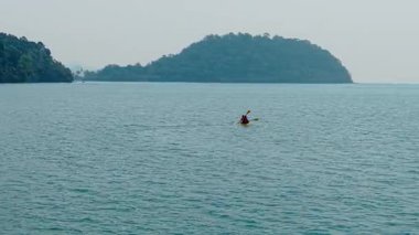 Tropik adaların yakınlarındaki sakin sularda kano süren iki kişi - 4K Yatay