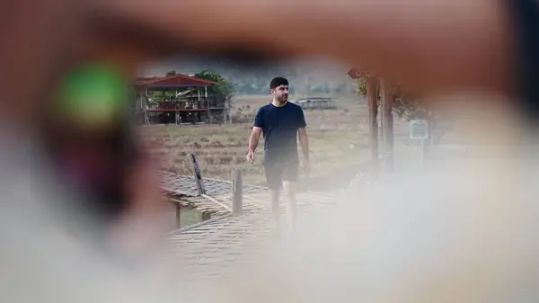 Güneydoğu Asya 'daki pitoresk kırsal bir bölgede barışçıl bir bambu köprüsünde yürüyüş yapan turist - 4K Yatay