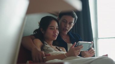 Genç çift yatakta birlikte vakit geçirmeyi seviyor, akıllı telefonlara bakıyorlar.