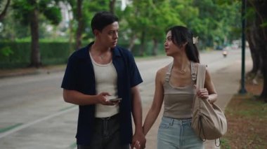 Genç çift el ele tutuşuyor ve şehir caddesinde yürürken navigasyon için akıllı telefon kullanıyor.