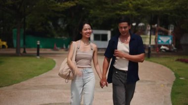 Birlikte yürüyen çiftler, yeşil park yaprakları arasında mahrem bir anı paylaşıyorlar.