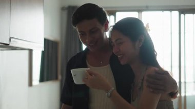 Neşeli ortaklar sıcak içecekleri paylaşır, mutfak tezgahının yanında durup gülümserler.