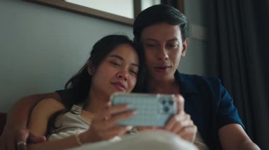 Yatak odasında dinlenirken bir çift uzanıp, akıllı telefon ekranını paylaşıyor.