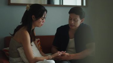 Genç çift oturma odasındaki kanepede ciddi ciddi konuşuyor, kişisel meseleleri tartışırken birbirlerine yaslanıyorlar.