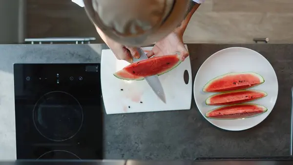 Şef modern bir mutfakta beyaz bir kesme tahtasıyla karpuz dilimleri kesiyor, ferahlatıcı bir yaz yemeği hazırlıyor.