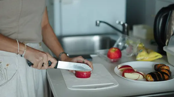 Beyaz kesim tahtasında kırmızı elmaları dilimleyen kadın modern mutfakta sağlıklı bir kahvaltı hazırlıyor.