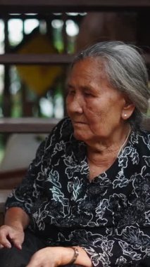 Yaşlı Taylandlı kadın ahşap bir evin basamaklarında derin derin oturur.