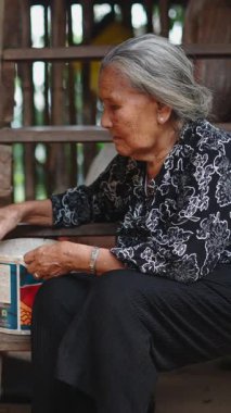 Yaşlı bir Asyalı lahu kadını merdivenlerde oturmuş tavukları besliyor.