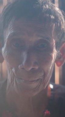 Güneş ışığı, bambu kulübesinde poz veren yaşlı bir Asyalı kadının yüzünü aydınlatıyor.