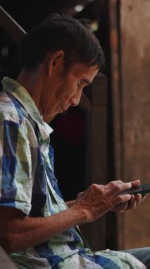 Lahu kabilesinin kıdemli adamı geleneksel verandada cep telefonu kullanıyor.