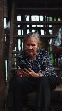 Yaşlı bir kadın ve yaşlı bir adam verandanın ahşap basamaklarında oturmuş akıllı telefonları kullanıyorlar.