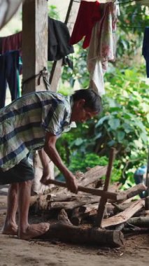 Kırsal kesimdeki FullHD dikey bir köyde verandanın altında yakacak odun kesen Lahu adamı.