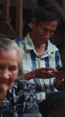 Yaşlı bir kadın ahşap basamaklarda, FullHD dikey otururken kıdemli adam akıllı telefon kullanıyor.