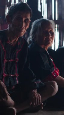 Lahu kabilesinden yaşlı bir çift yakacak odunla yemek pişirirken yerde oturuyor.