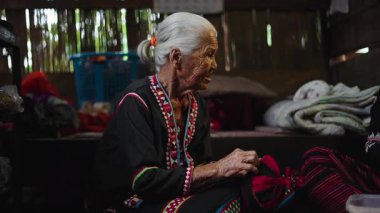 Yaşlı bir Asyalı zanaatkar bronzlaşmış elleriyle titizlikle bir tekstil yaratımı üzerinde çalışıyor. 4K Yatay.