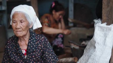 Başörtüsü takan düşünceli yaşlı bir kadının portresi kırsal alanda çalışan başka bir kadını izliyor - 4K Yatay