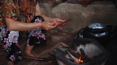 Yaşlı Vietnamlı bir kadın alevleri yanık tutmak için küçük bir odun parçası ekliyor - 4K Yatay